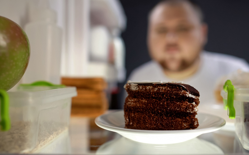 Ein Mann mit Übergewicht öffnet einen Kühlschrank, weil er seine schlechte Stimmung mit dem Konsum von Nahrungsmitteln verbessern möchte.