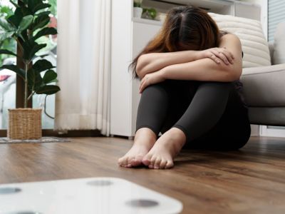 Eine Frau mit depressiver Verstimmung sitzt vor einer Wage und ist unzufrieden mit ihrem Körpergewicht.