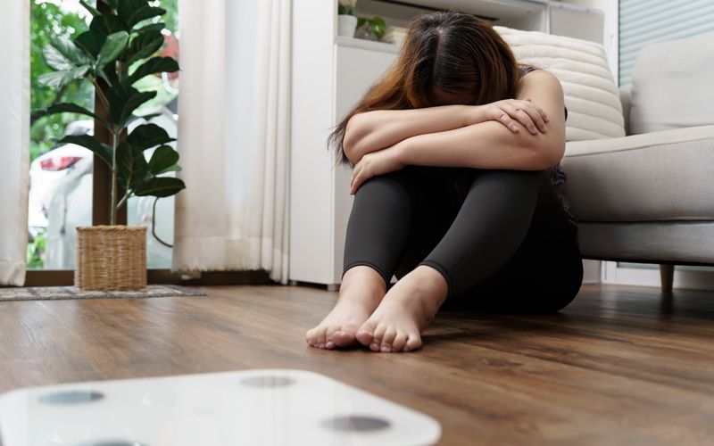 Eine Frau mit depressiver Verstimmung sitzt vor einer Wage und ist unzufrieden mit ihrem Körpergewicht.